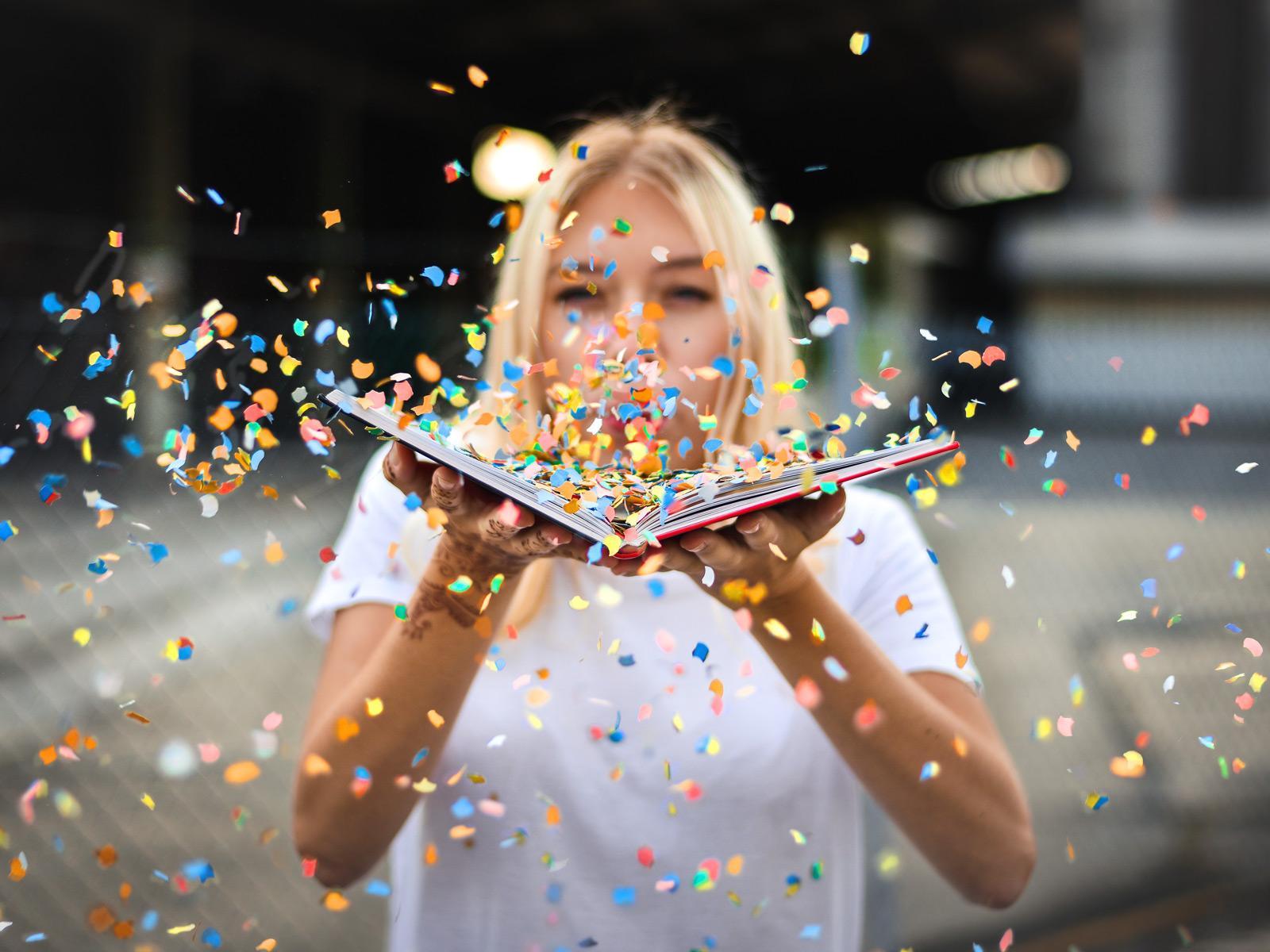 A woman blows confetti from an open book © Paul Stachowiak/Pixabay