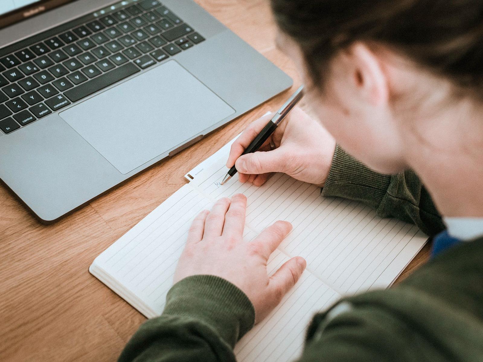 A young woman writes notes in a notebook in front of a laptop computer © Hagar Lotte Geyer/Pixabay