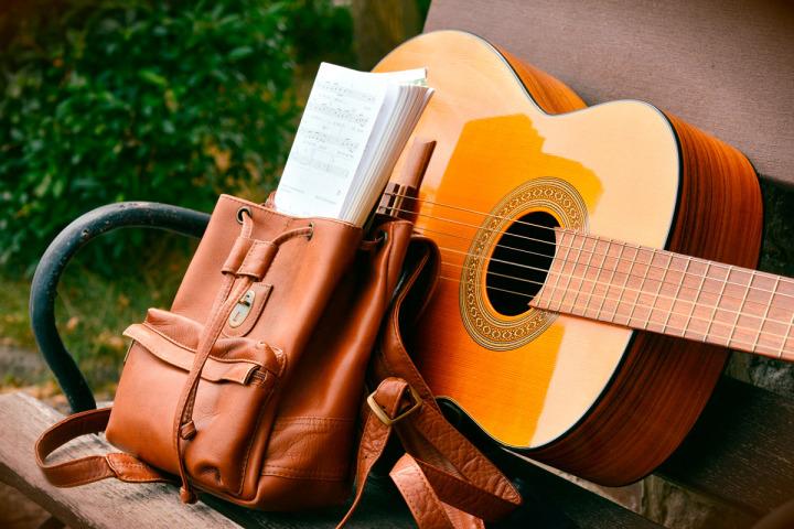 Eine Gitarre und ein geöffneter Rucksack mit Noten auf einer Bank © Congerdesign/Pixabay
