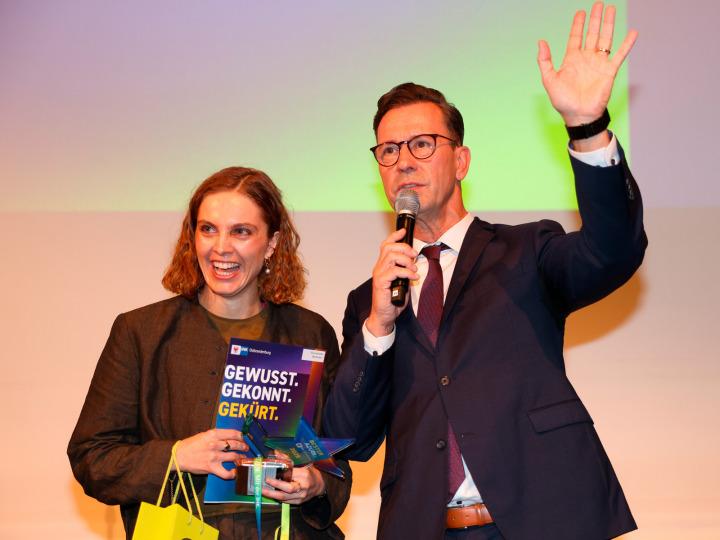 Elisa Karlotta Beckmann freut sich neben dem Moderator des Abends, Mario Schmidt, über ihre Auszeichnung. Die junge Frau hat die Ausbildung zur Industriekeramikerin Modelltechnik bei der GOLEM – Kunst und Baukeramik GmbH abgeschlossen. Sie ist in ihrem Ausbildungsberuf Bundesbeste und gleichzeitig mit 97 Punkten auch die beste Absolventin im gesamten Kammerbezirk Ostbrandenburg. © Marco Kümpfel | IHK Ostbrandenburg