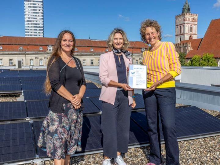 Viadrina-Vizepräsidentin Janine Nuyken (r.) mit der Geschäftsführerin der Industrie- und Handelskammer Ostbrandenburg, Monic Zweig (M.), und der Beauftragten für Nachhaltigkeit an der Viadrina, Sahra Damus, vor der Photovoltaikanlage auf dem Dach des Auditorium Maximum in Frankfurt (Oder)
